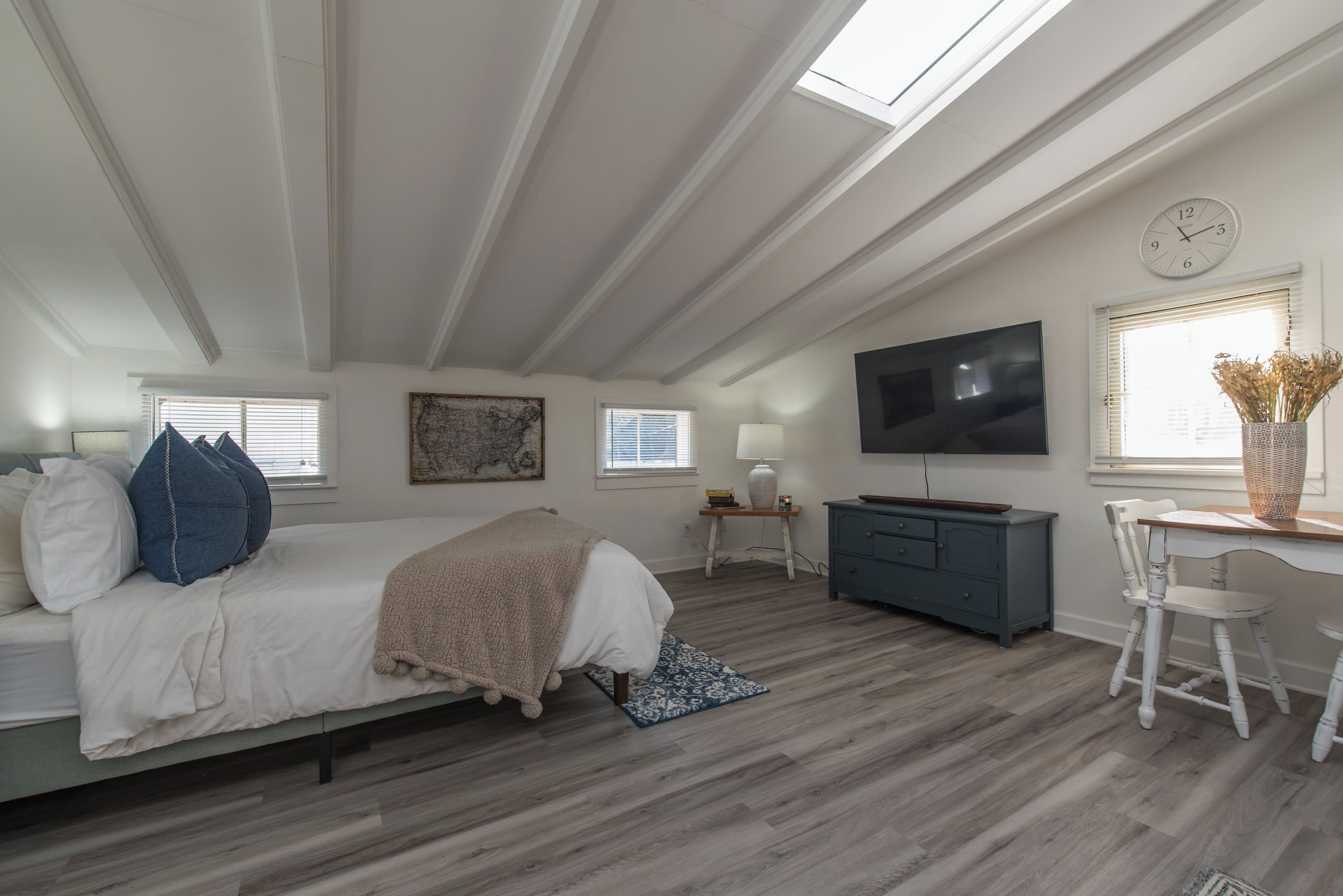 Un dormitorio con cama, escritorio, televisor y ventana con reloj.