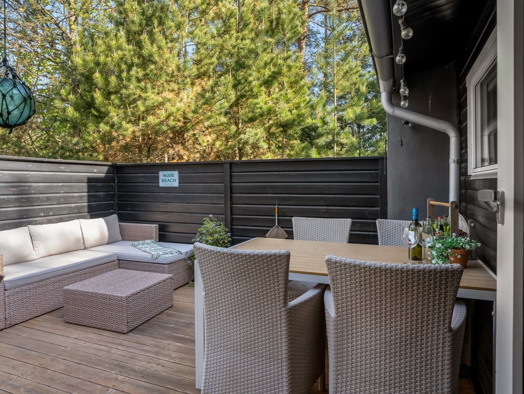 Una terraza con mobiliario de mimbre, una mesa y un letrero que dice 'NUDE BEACH'.