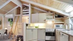 A compact kitchen with white cabinets, a built-in microwave, and a dishwasher. A wooden ladder is visible, suggesting a lofted space.