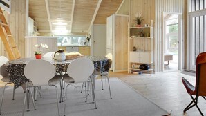 A modern kitchen with wooden beams, a dining area with a table and chairs, and a view of the outdoors through a large window.