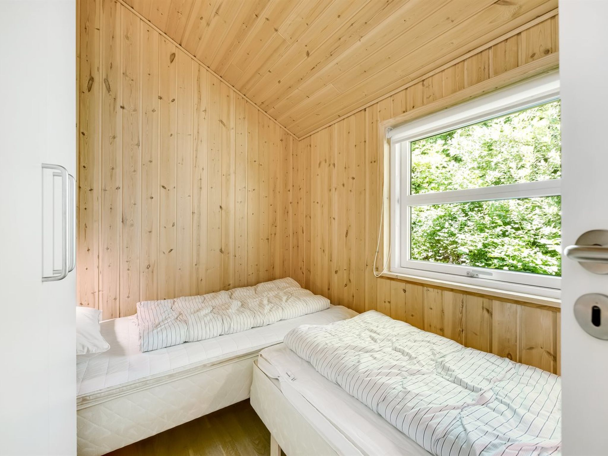 A small, wooden-paneled room with two beds and a window overlooking greenery.