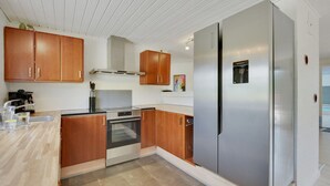 A modern kitchen with wooden cabinets, stainless steel appliances, and a tiled floor. - "Jorkin" - 1.8km from the sea by Interhome (Ulfborg)