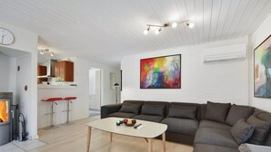 A modern living room with a sofa, a coffee table, and a fireplace. There is a kitchen area with a bar stool and a colorful painting on the wall. - "Jorkin" - 1.8km from the sea by Interhome (Ulfborg)