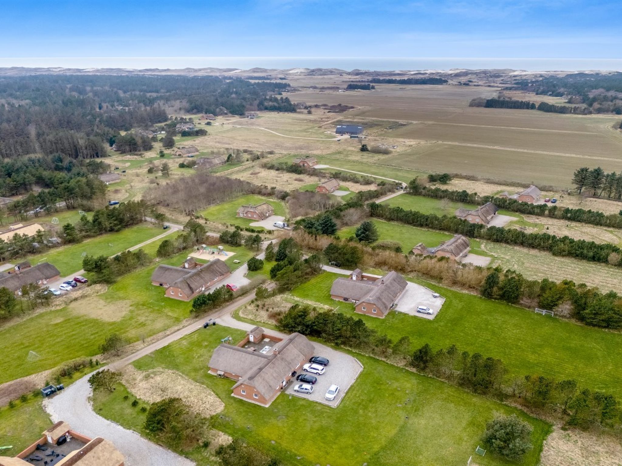 An aerial view of a residential area with houses, green lawns, and a clear sky.