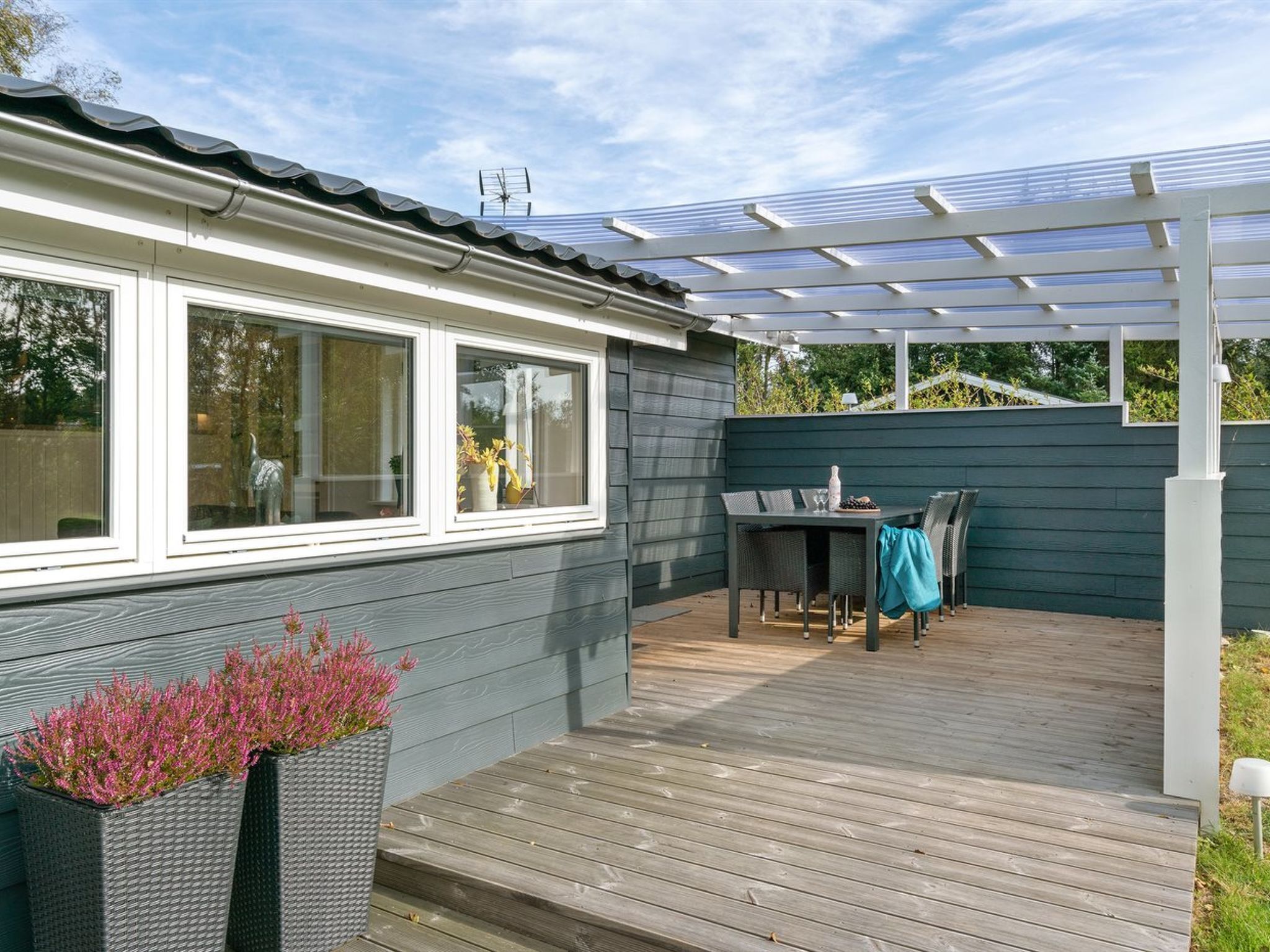 A covered patio with a table and chairs, a pergola, and a view of a house with windows and a fence.