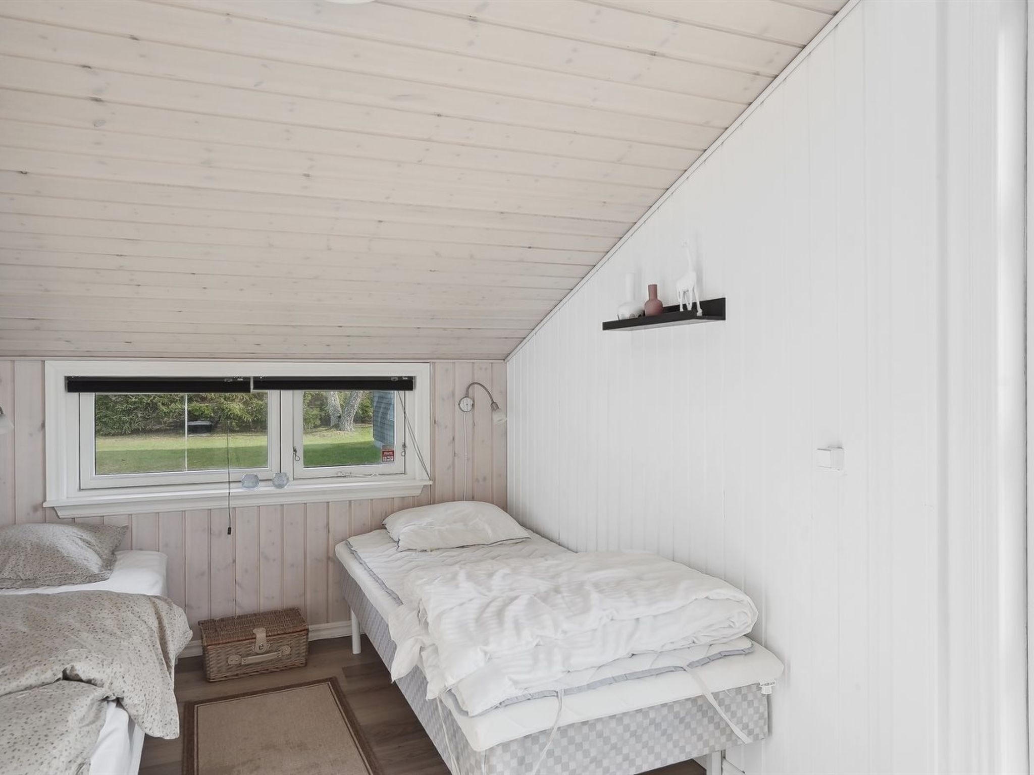 A bedroom with two beds, a window, and a shelf with decorative items.