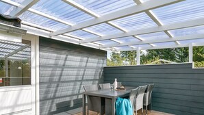 Un patio couvert avec une table et des chaises, une terrasse en bois et une structure de toit en verre.