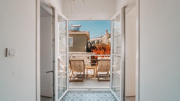 A corridor leading to a balcony with a tiled floor, two chairs, and a table. - Mea Reisdere (Cesme)
