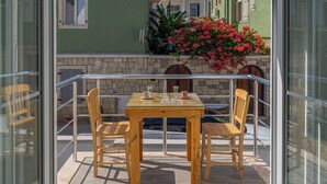 An outdoor wooden table with chairs, a glass railing, and a view of a building with a stone wall and a flower box. - Mea Reisdere (Cesme)