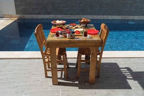 A dining table with a pool view, surrounded by wooden chairs. - Mea Reisdere (Cesme)