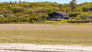 A coastal house with a deck, surrounded by a grassy field and dense trees.