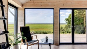 A modern interior with a large window, a wooden ceiling, and a view of a green field.