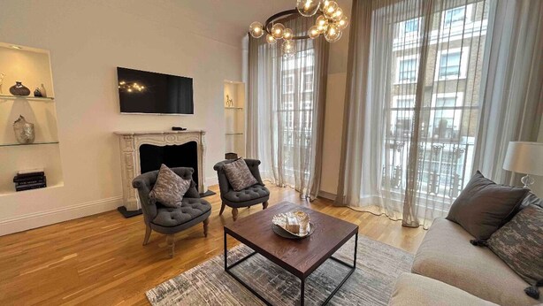 A modern living room with a fireplace, two armchairs, a coffee table, and a television on the wall.