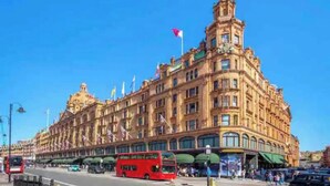 A large, ornate building with multiple flags, a prominent entrance, and a red double-decker bus in front.