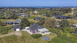 Vista aérea de una zona residencial con casas, una casa grande con invernadero de cristal y vista al mar.