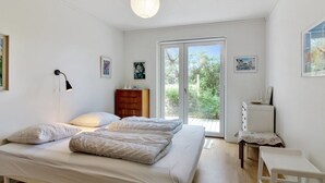 Un dormitorio con cama, mesita de noche, cómoda y ventana con vistas a follaje.