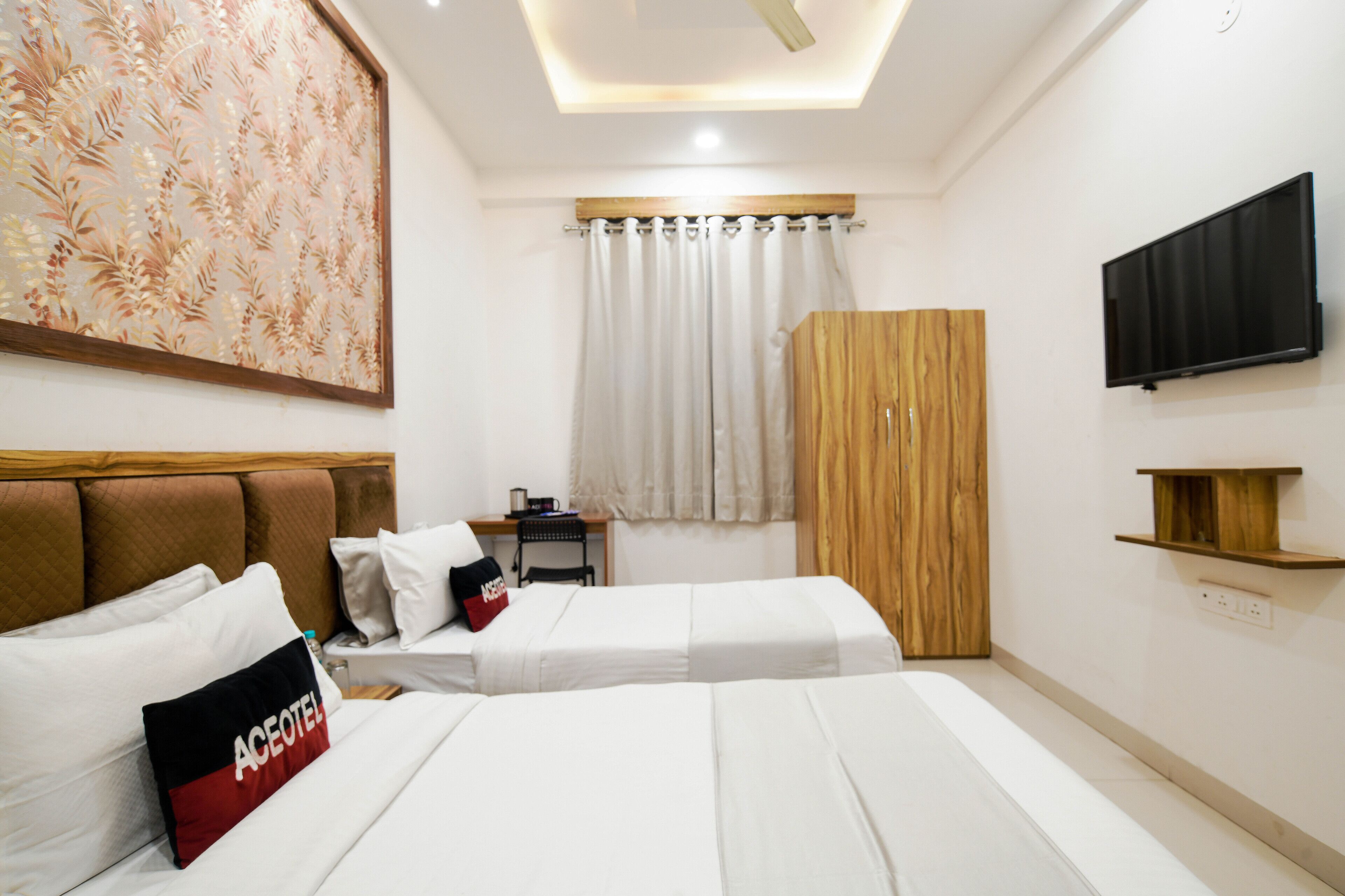 A hotel room with two beds, a wooden wardrobe, a flat-screen TV, and a desk with a chair.