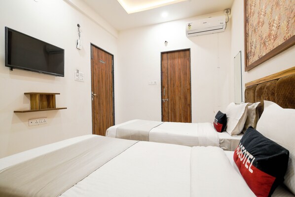 A hotel room with two beds, a flat-screen TV, wooden doors, and a painting on the wall.