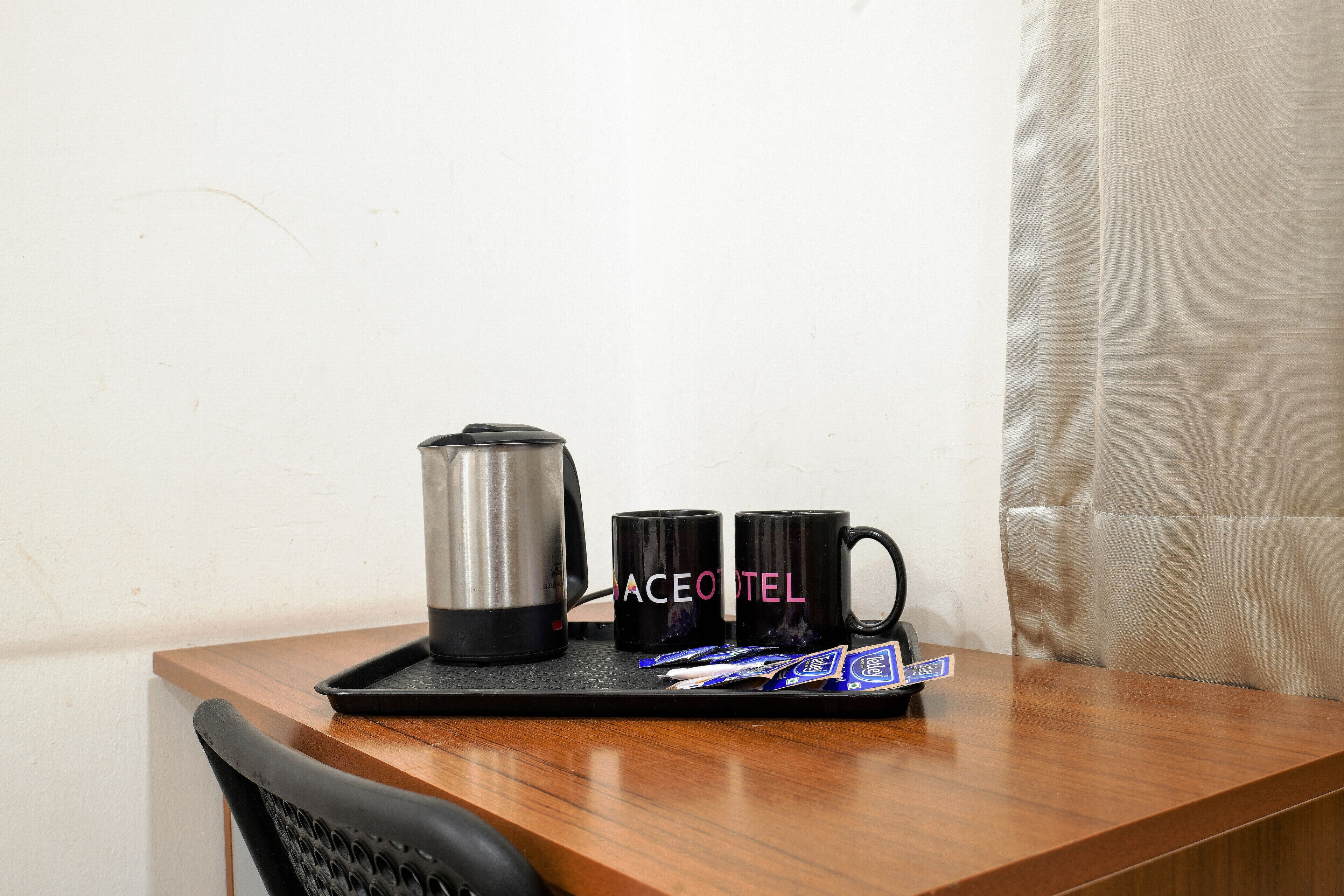 A small table with a coffee maker, two mugs, and a tray with packets.