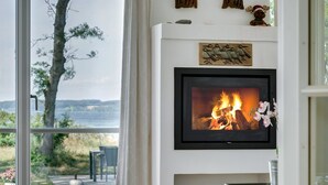 Una sala de estar con chimenea, un ventanal con vistas al exterior y un televisor montado en la pared.