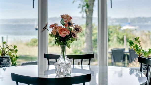 Una mesa con un jarrón de vidrio transparente que contiene flores, con vistas panorámicas a través de amplios ventanales.