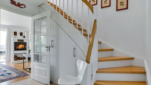 Una escalera moderna con escalones de madera y paredes blancas, que conduce a una habitación con chimenea y cuadros en la pared.