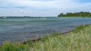 Un lago tranquilo con barcos, orillas cubiertas de hierba y una costa lejana.