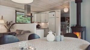 Un salon chaleureux avec une table ronde, une cheminée et un coin cuisine doté de meubles blancs et d’une cuisinière.