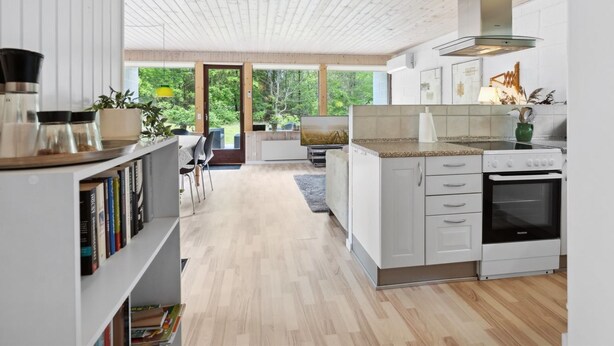 Une cuisine moderne avec des meubles blancs, une cuisinière encastrée et une grande fenêtre donnant sur un espace verdoyant.