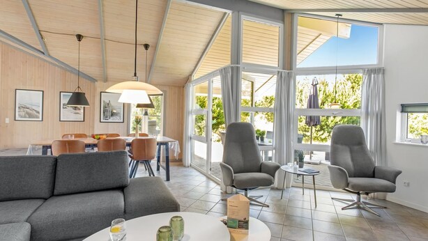 Amplia sala de estar con techo alto, ventanas grandes y zona de comedor con mesa y sillas.
