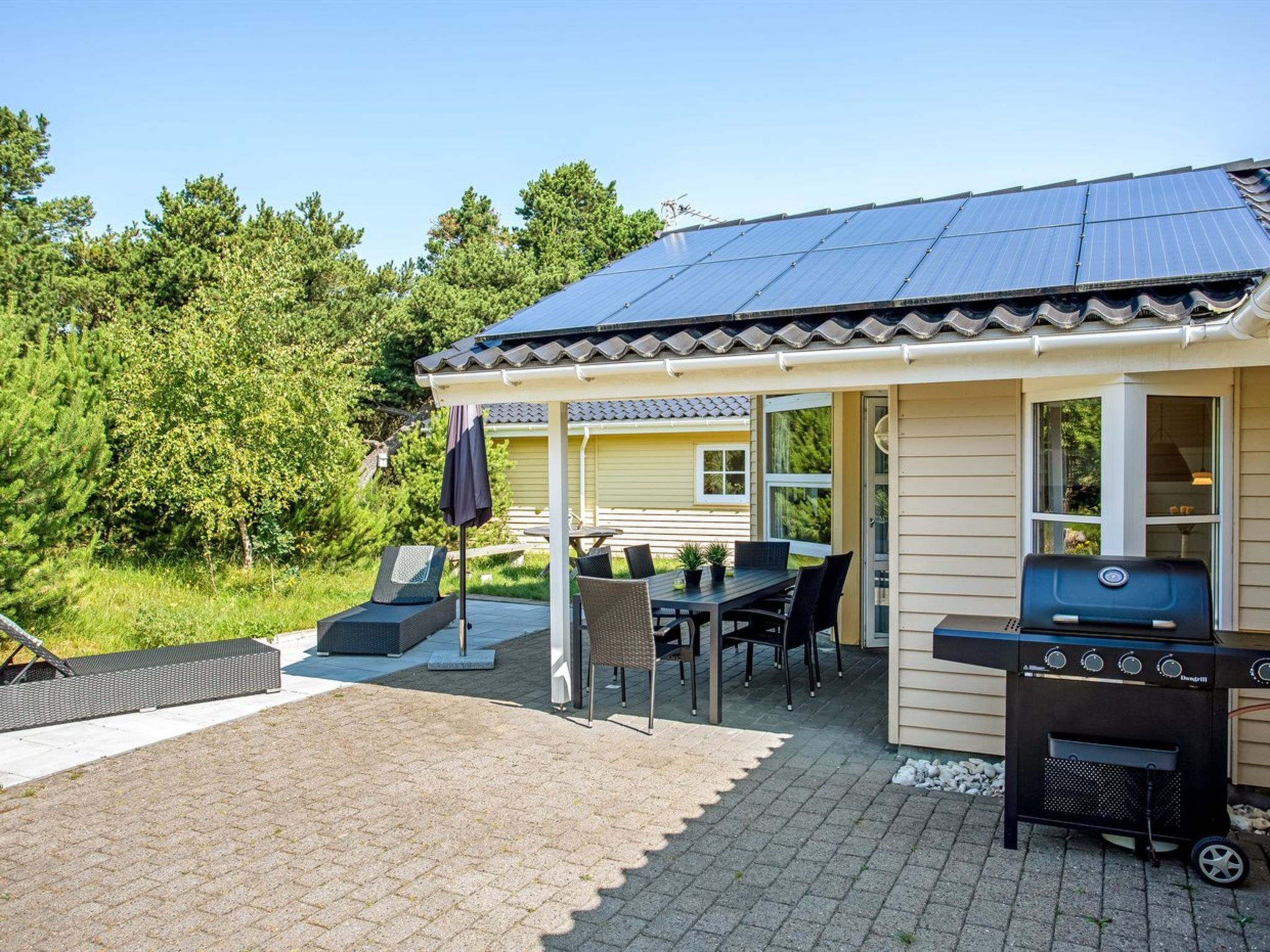 Un patio techado al aire libre con una mesa y sillas para comer, una parrilla y una pérgola con una mesa y sillas debajo.