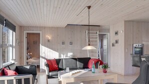 Ein modernes Wohnzimmer mit Holzbalkendecke, einer schwarzen Ledersofa, einem weißen Couchtisch und einem Essbereich mit weißem Tisch und Stühlen.