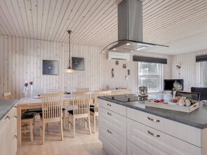 Une cuisine moderne avec des murs recouverts de panneaux en bois, un îlot central et un coin repas avec des chaises en bois.