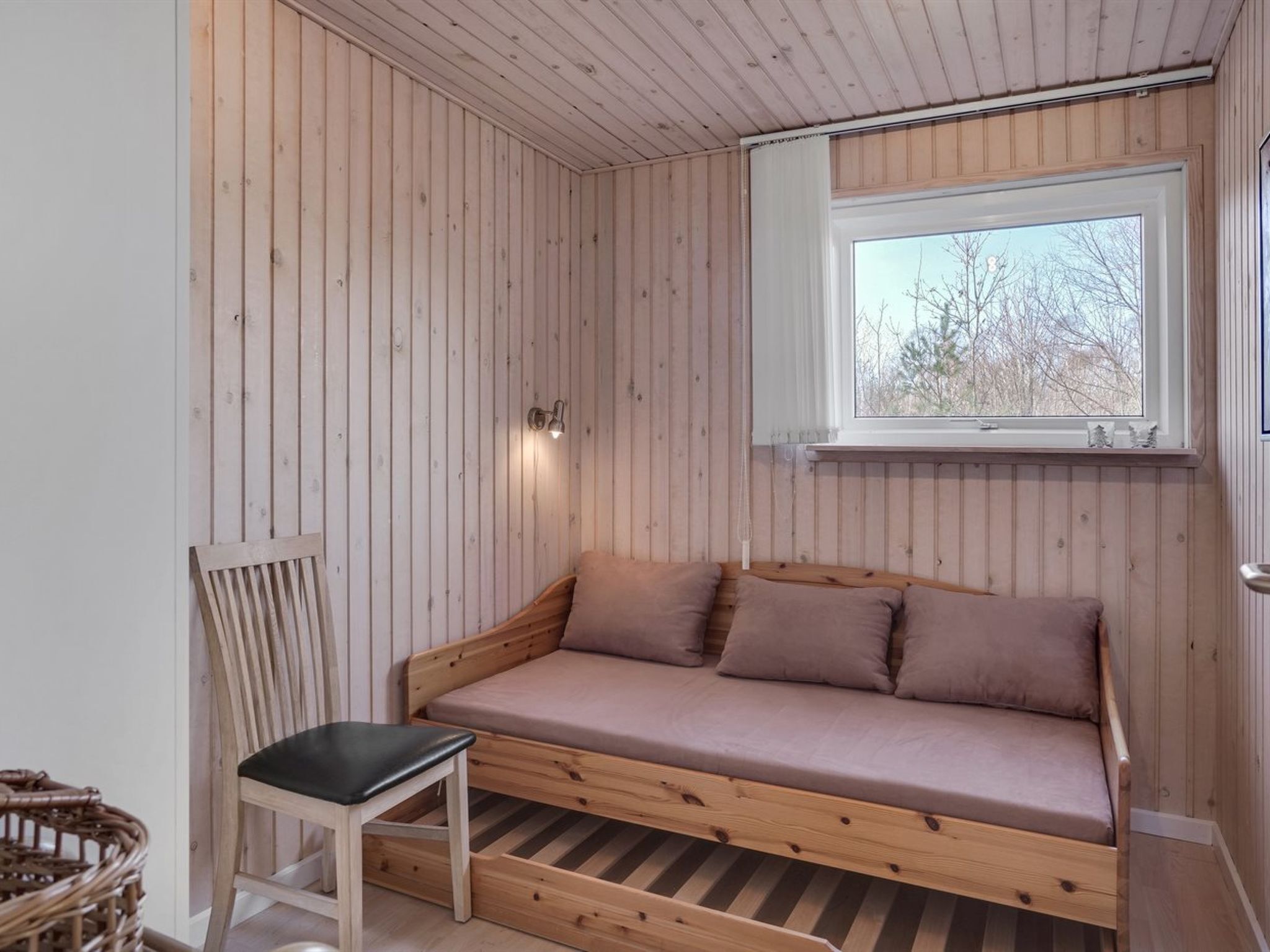 Une pièce chaleureuse avec un mur lambrissé en bois, une fenêtre offrant une belle vue, un banc en bois et un coin salon confortable avec des coussins.