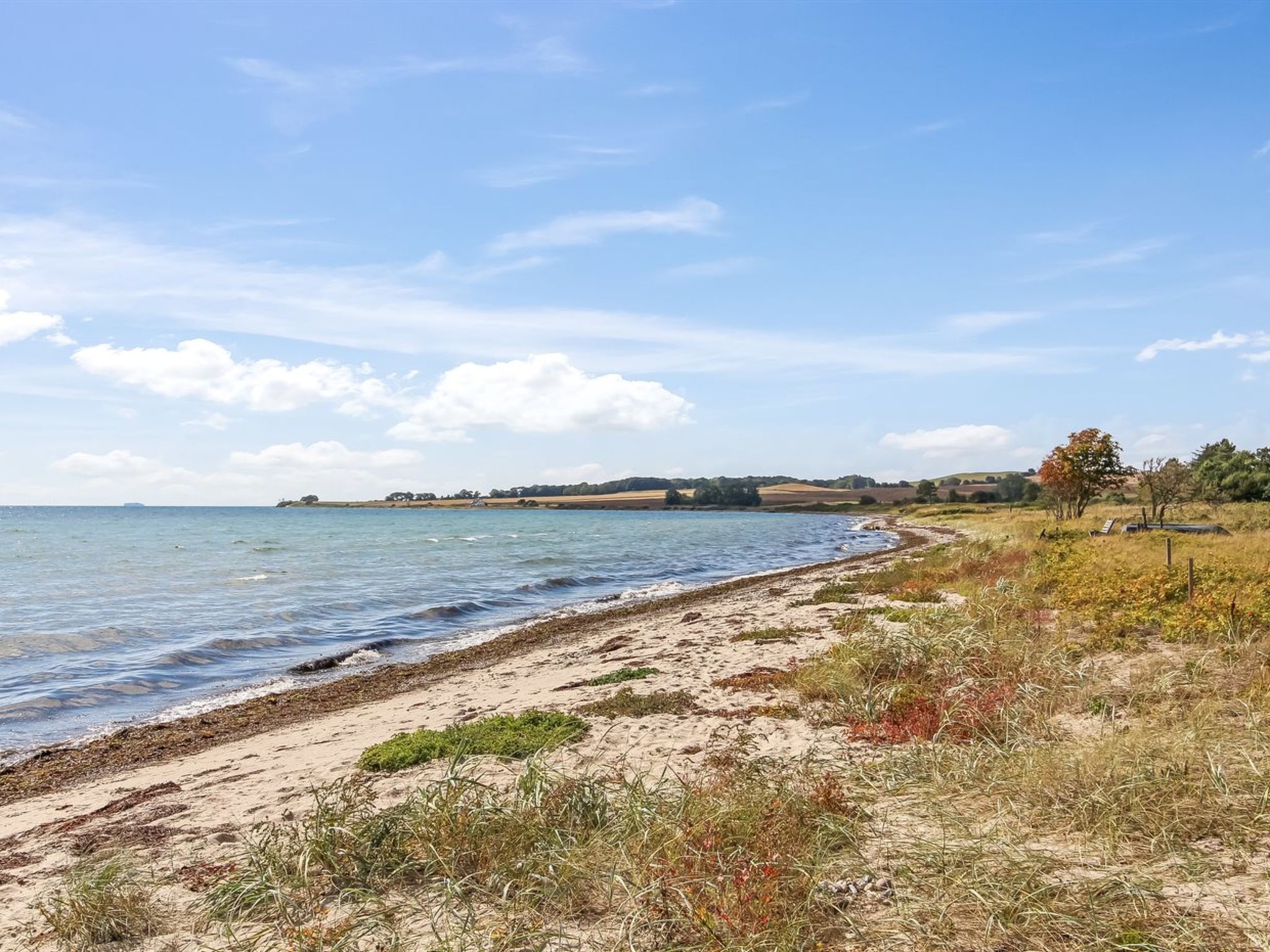 Un paysage côtier avec une plage de sable, une mer calme et des collines à l’horizon.