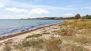 Een kustlandschap met een zandstrand, kalme zee en verre heuvels.