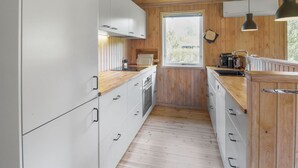 Een moderne keuken met houten wanden en witte kasten, een raam en een hanglamp.