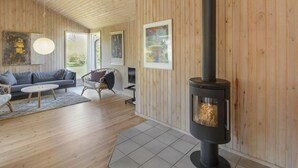 Een gezellige woonkamer met houten inrichting, een bank, een fauteuil, een bijzettafeltje en een open haard.