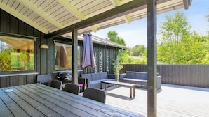 Een terras buiten met een houten dek, een barbecue en zitplaatsen.
