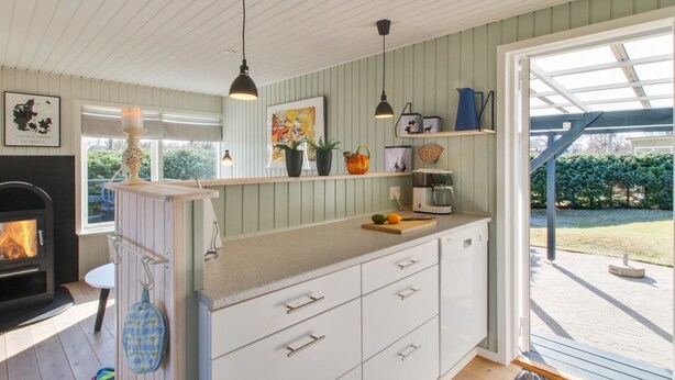 Une cuisine moderne avec des armoires blanches, une cuisinière encastrée, des luminaires suspendus et une vue sur le jardin grâce à une porte vitrée.