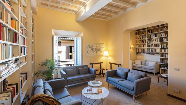 A spacious living room with a high ceiling, built-in bookshelves, a sofa set, a coffee table, and a lamp.