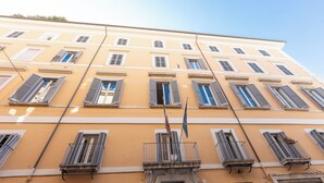 A multi-story building with a yellow facade, multiple windows with shutters, and a balcony with a metal railing.