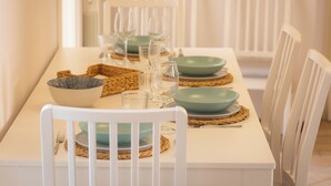 A dining table set with plates, bowls, and glasses, surrounded by white chairs.