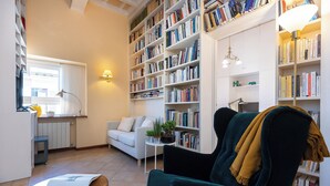 A cozy living room with a green armchair, a white sofa, and a bookshelf filled with books.