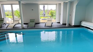 Une piscine intérieure à l’eau d’un bleu cristallin, entourée de murs blancs et de grandes fenêtres.