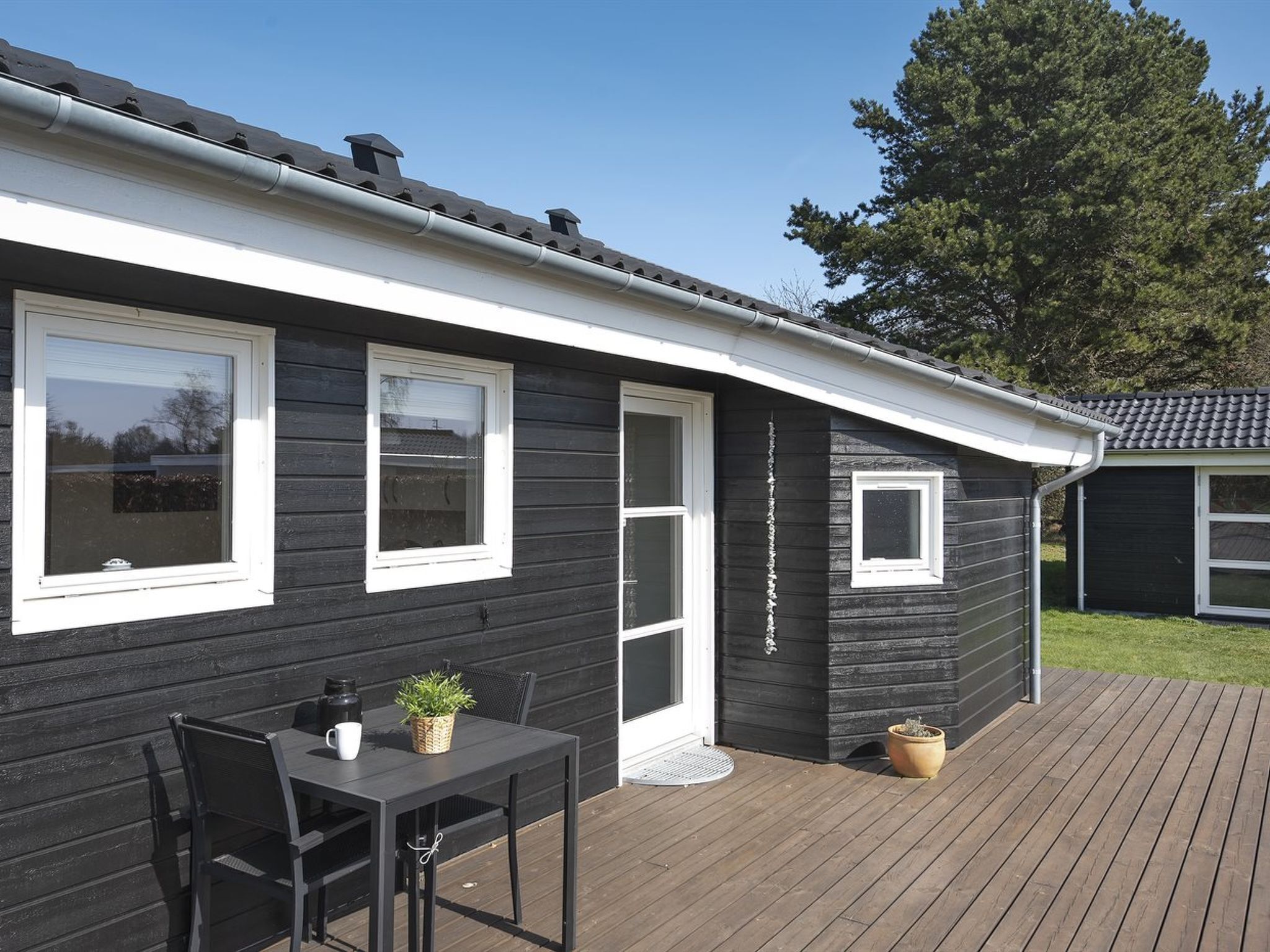 Ein schwarzes Haus mit weißem Zierstreifen, einer Terrasse und einem kleinen Garten.