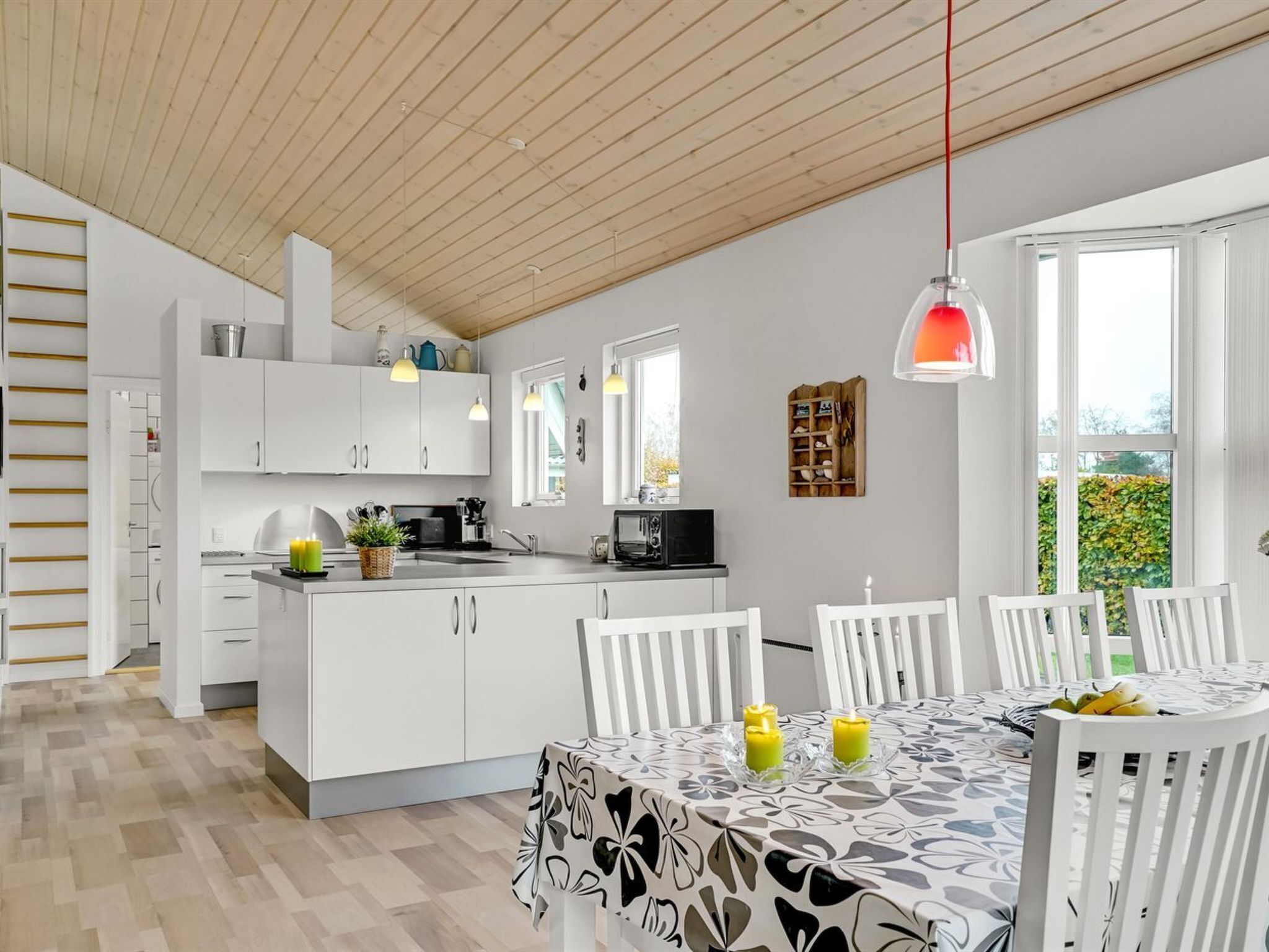 Een moderne keuken met witte kasten, een eethoek met een tafel voor vier personen, en een groot raam met uitzicht op groen.