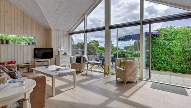 Ein geräumiges Wohnzimmer mit einer großen Glaswand, Holzvertäfelung, einem Fernseher und einem Essbereich.