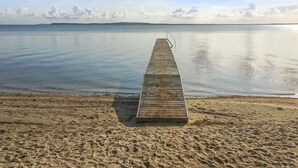Eine hölzerne Pier, die sich in ruhiges Wasser erstreckt, mit einem wolkenlosen Himmel darüber.