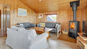 Interior acogedor de una cabaña, con paredes de madera, un sofá, una mesa de comedor y una estufa de leña.